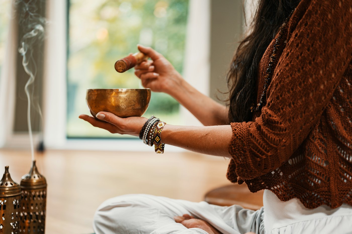 Hands striking a brass singing bowl beside burning incense